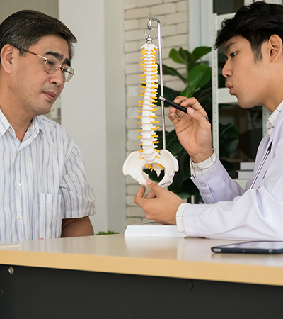 Chiropractor pointing at spine bone model, explaining the problem to mature female patient. Chiropractor pointing at spine bone model, explaining the problem to mature female patient.