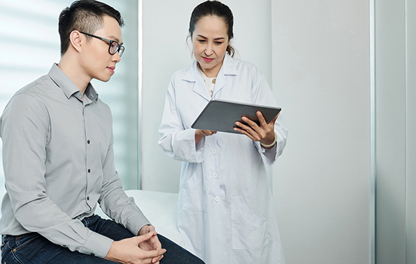 Male-patient-with-chiro-discussing-NF-Chiropractic Female-Chiropractor-Holding-onto-a-Tablet-Explaing-Report-to-Patient-NoFrills-Chiropractic-Singapore