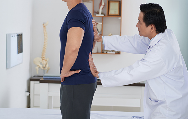 White-Coat-Male-Chiropractor-Touching-Male-Patients-Back-NoFrills-Chiropractic-Singapore
