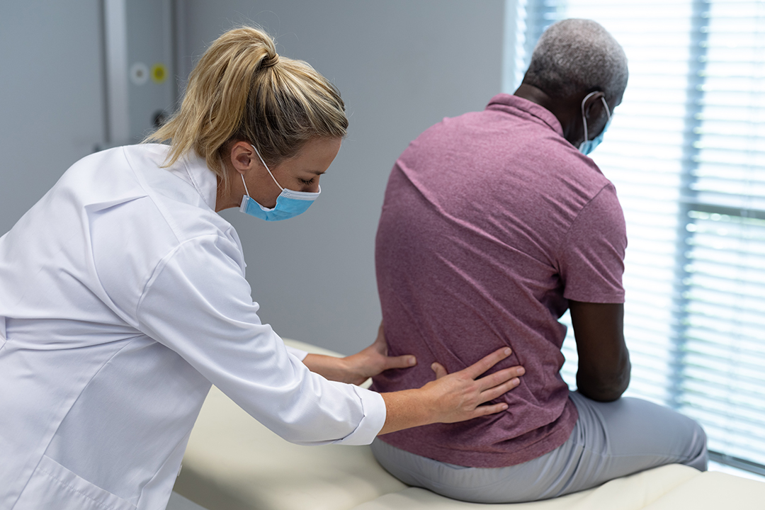 female chiropractor wearing mask palpating back of african american male patient. medicine, health and healthcare services during coronavirus covid 19 pandemic.