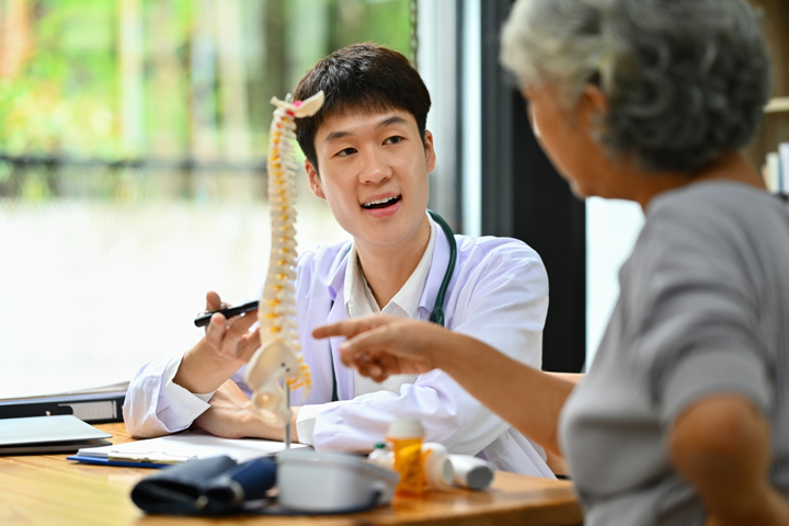 Male chiropractor explaining structure of spine to mature female patient in clinic. Health care concept. Male chiropractor explaining structure of spine to mature female patient in clinic. Health care concept.